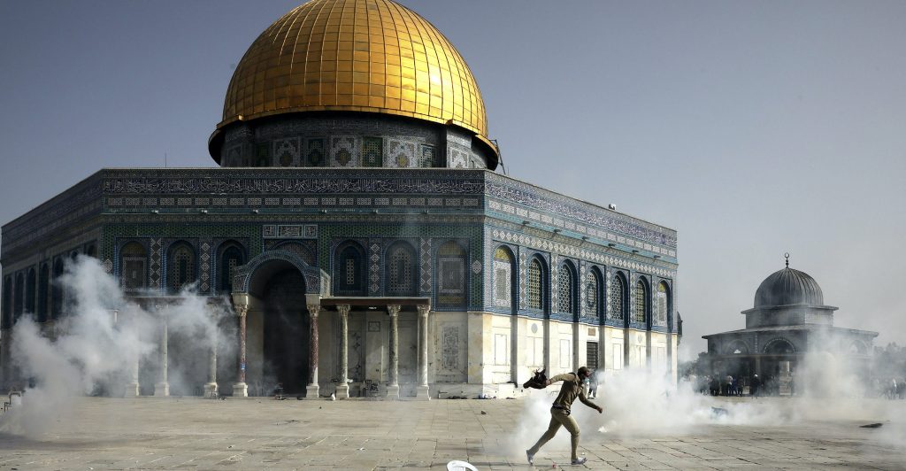 A Palestinian man runs away from tear gas during clashes with Israeli security forces in front of the Dome of the Rock Mosque at the Al Aqsa Mosque compound in Jerusalem's Old City Monday, May 10, 2021. Israeli police clashed with Palestinian protesters at a flashpoint Jerusalem holy site on Monday, the latest in a series of confrontations that is pushing the contested city to the brink of eruption. Palestinian medics said at least 180 Palestinians were hurt in the violence at the Al-Aqsa Mosque compound, including 80 who were hospitalized. (AP Photo/Mahmoud Illean)